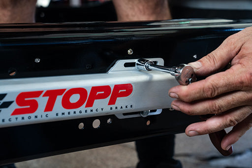 A person's hand using a socket wrench to tighten one of the bolts holding an E-Stopp actuator to a chassis frame rail