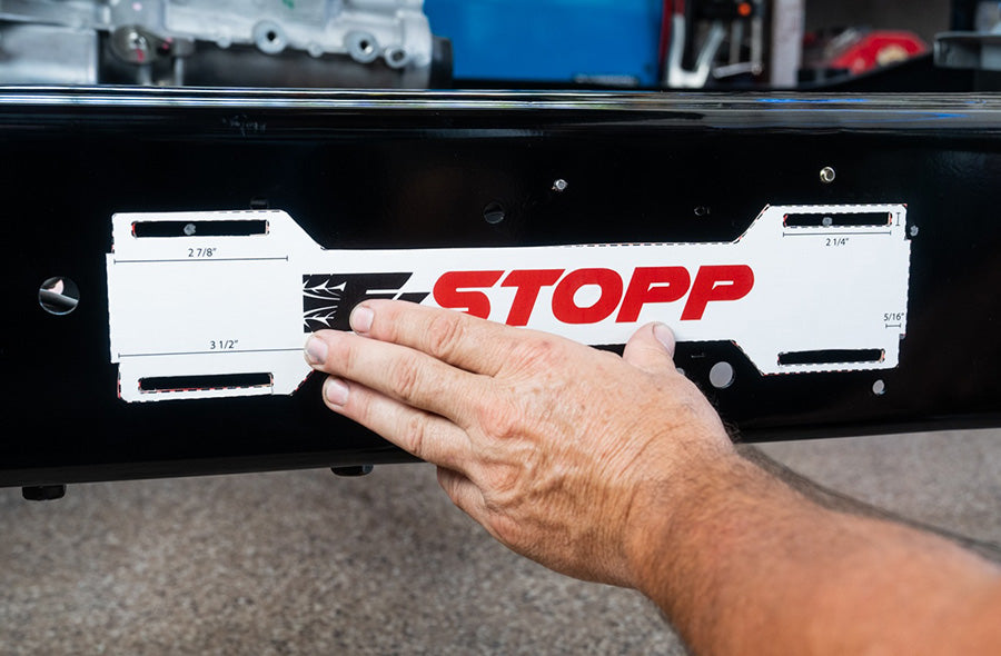 Person holding cardboard E-Stopp actuator template up to chassis frame rail